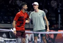 Two tennis players shake hands over the net on an indoor court