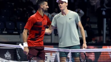 Two tennis players shake hands over the net on an indoor court