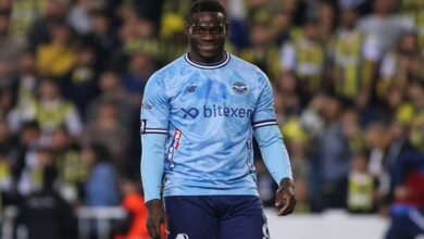 A soccer player dressed in a blue jersey stands on a grassy field