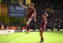 Two soccer players leap into the air on a vibrant green field.