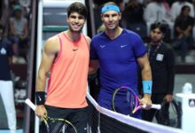 Two tennis players stand smiling at the net, each holding a racket