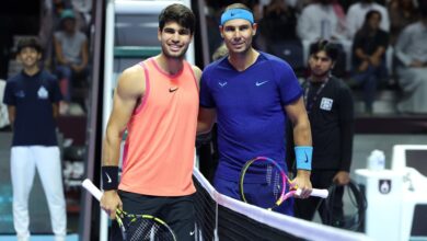 Two tennis players stand smiling at the net, each holding a racket