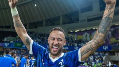 A soccer player joyfully celebrates his team's victory, raising his arms in triumph on the field