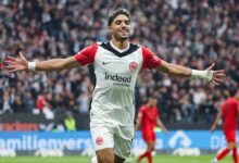 A soccer player joyfully celebrates after scoring a goal, raising arms in triumph on the field.