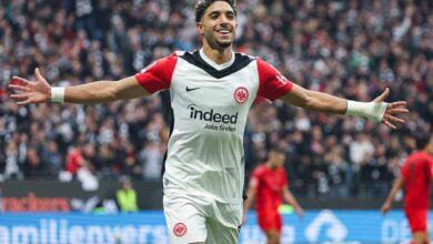 A soccer player joyfully celebrates after scoring a goal, raising arms in triumph on the field.