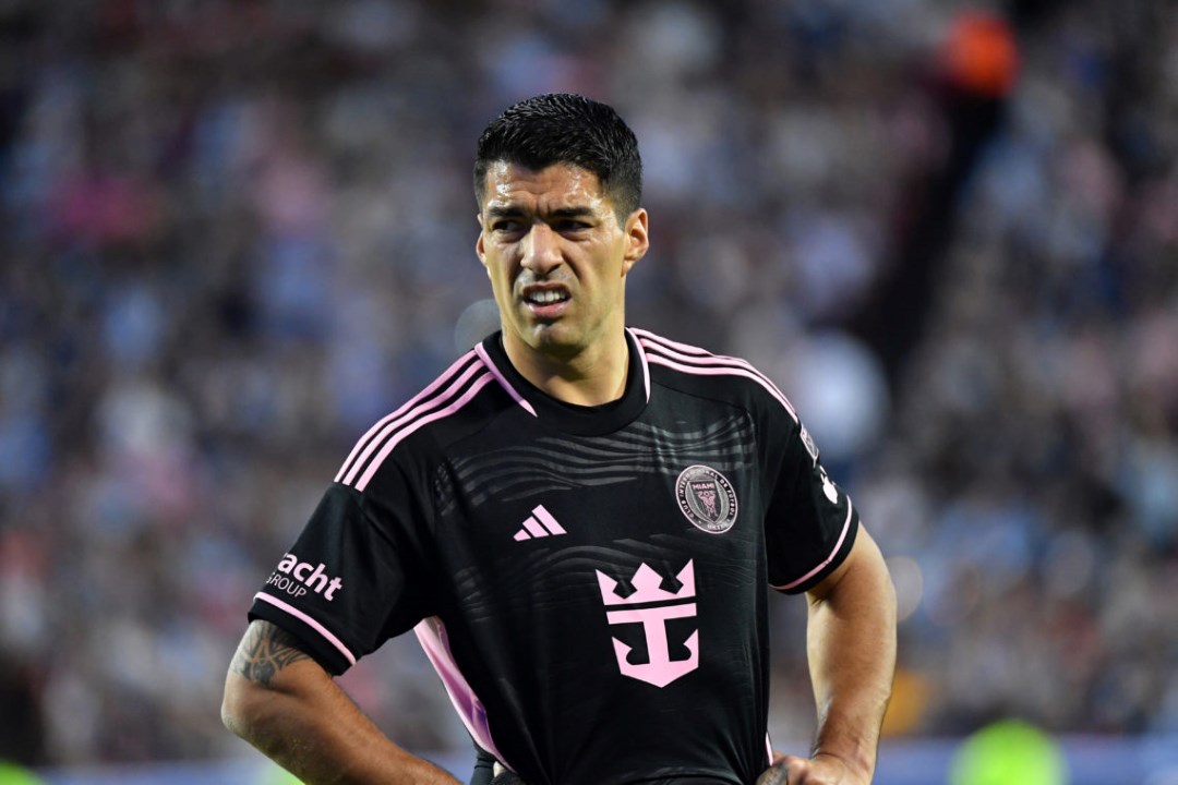 A soccer player wearing a pink shirt and black shorts is poised to kick the ball on the field