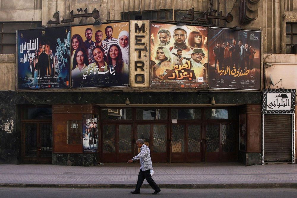 A man strolls by a movie poster in the bustling streets of Cairo.