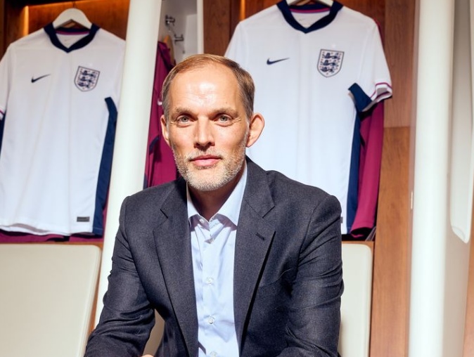 A man in a suit seated before a wall adorned with various England football shirts.