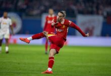 A man in red athletic gear skillfully kicks a soccer ball on a vibrant green field