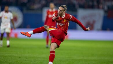 A man in red athletic gear skillfully kicks a soccer ball on a vibrant green field