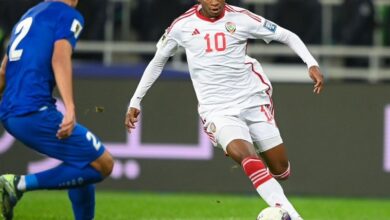 A soccer player in a white uniform sprinting while dribbling a ball on the field