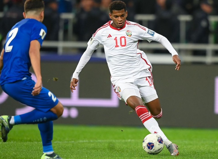 A soccer player in a white uniform sprinting while dribbling a ball on the field