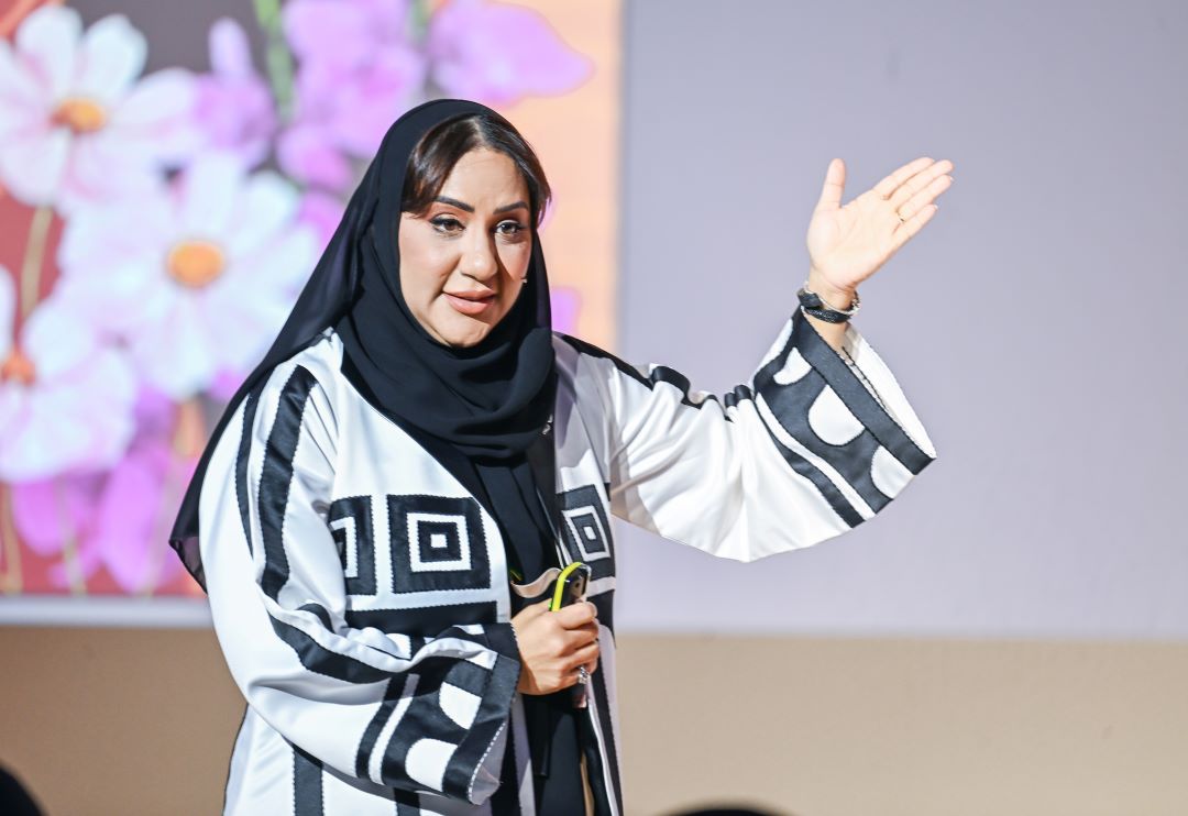 "A person in a black and white outfit speaking with a floral background."