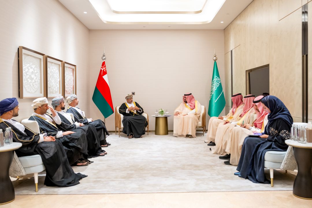 "Meeting between Omani and Saudi officials with flags in background."