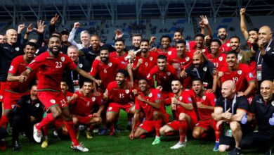 "Soccer team celebrating a win on the field, wearing red uniforms and numbers."