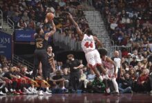 A basketball player takes a shot while a cheering crowd watches