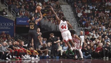 A basketball player takes a shot while a cheering crowd watches