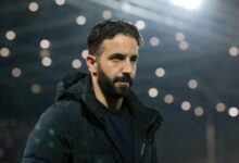 Ruben Amorim in a black jacket stands confidently in front of a large stadium