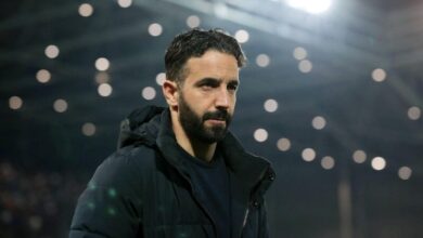 Ruben Amorim in a black jacket stands confidently in front of a large stadium